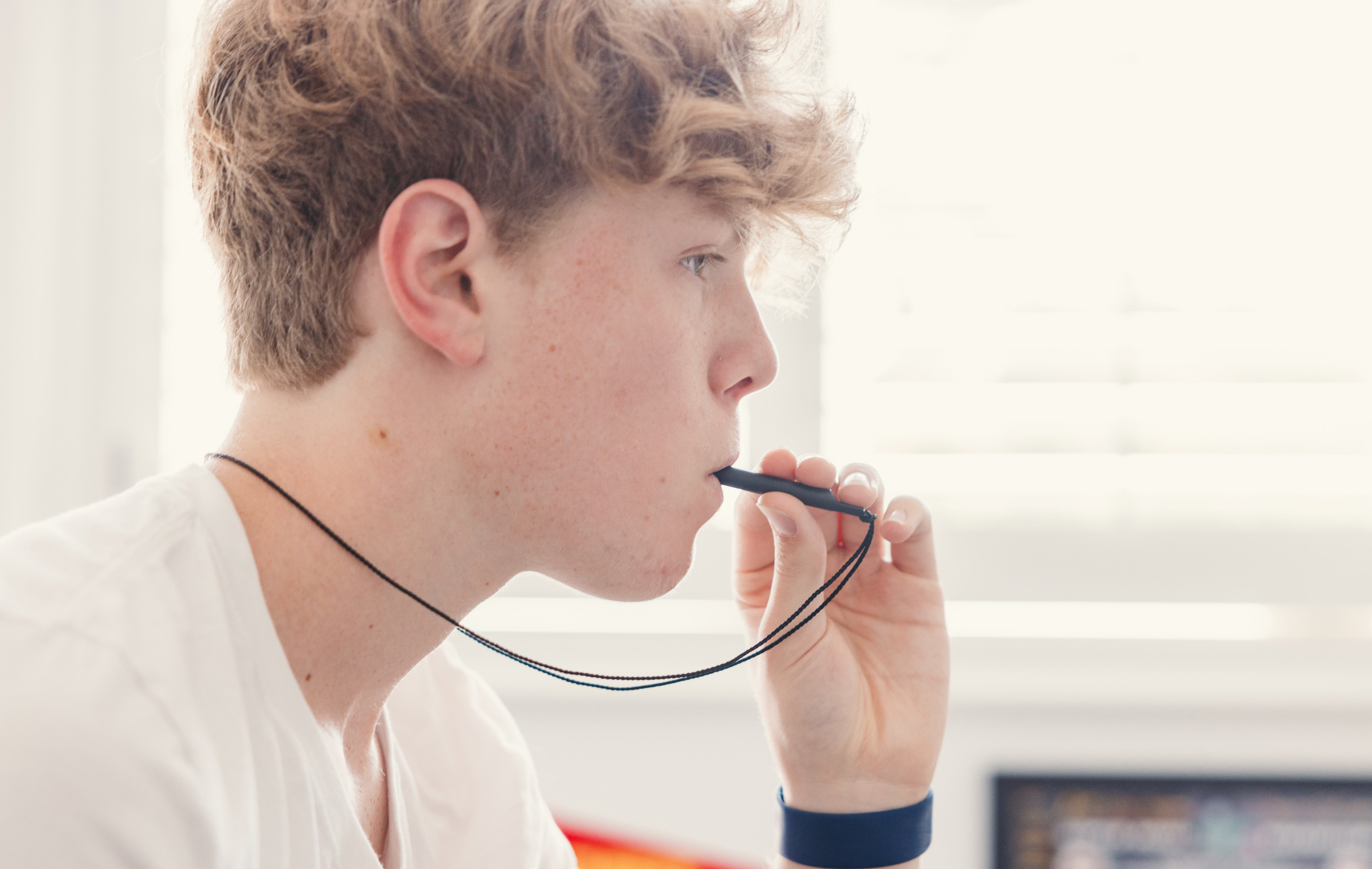 Teenager holding the Komuso Active Shift breathing necklace while looking into the distance, pausing for a micro-calming breathing moment.